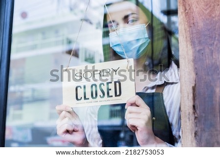 Caucasian coffee owner wear mask due pandemic, turns sorry closed sign. Attractive young girl waiter closed sign to shut down business due to financial crisis from COVID-19 lockdown and quarantine.