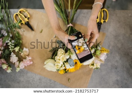 Hands of florist holding smartphone taking picture of bouquet of different flowers on counter. Flat lay, top view mockup. Floristics, business, decoration concept. Close up.