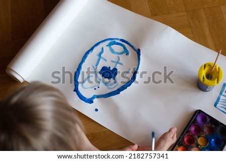 a boy is drawing a face with blue watercolor, flatlay