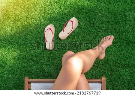 Selective focus of a girl sitting in a hammock on artificial turf with bare feet and flip-flops on the grass Royalty-Free Stock Photo #2182767719