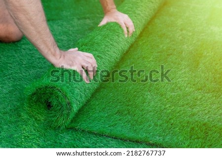 Selective focus on a man's hands unrolling a roll of artificial turf. Easy laying of artificial green grass Royalty-Free Stock Photo #2182767737