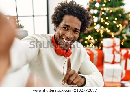 Young african american man making selfie by the camera sitting by christmas tree at home.