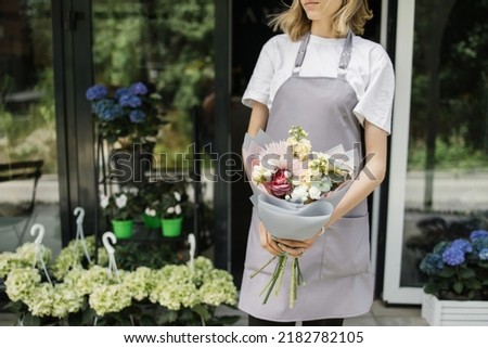 Cropped hands with bouquet near flower shop door. Photo of b woman standing in front of flower shop. Female florist outside shop. Woman working at flower shop.