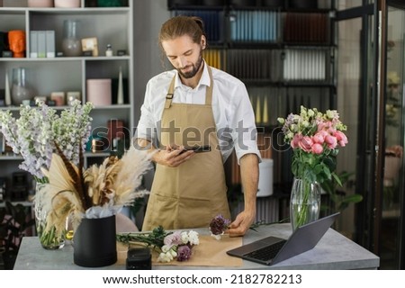 Portrait of young male florist making fashion modern bouquet of different flowers on counter and taking photo on smartphone for social media. Masterclass. Gift for bride on wedding, mother women's day