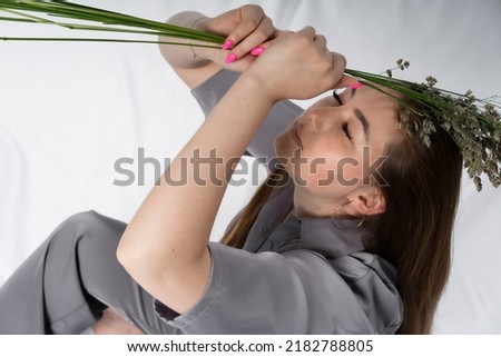 young woman in a gray satin, trendy, trouser suit with herbs. beautiful stylish photos in minimalism. white Studio. herbs. beauty. beauty, fashion concept