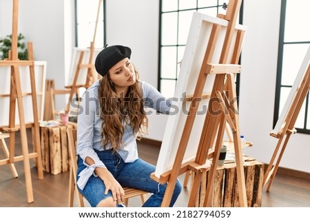 Young hispanic artist woman painting on canvas at art studio looking sleepy and tired, exhausted for fatigue and hangover, lazy eyes in the morning. 