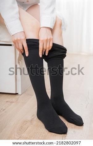 Black compression stockings on a woman in a white room. Black tights. Girl putting on stockings at home. Beautiful female legs.