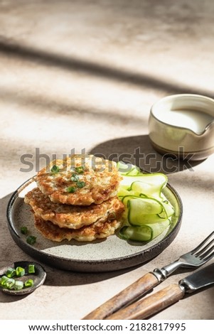 Vegetarian zucchini fritters with green onion, cucumber and cream sauce with shadows in hard light. Text space. Vertical orientation Royalty-Free Stock Photo #2182817995