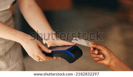 Unrecognizable customer scanning her credit card on a card machine to pay her bill in a cafe. Woman doing a cashless and contactless transaction using NFC technology. Royalty-Free Stock Photo #2182832297