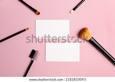 Makeup brush and white business card on pink background. A horizontal template for a makeup artist's business card or flyer design, with copy space