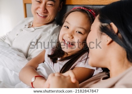 Happy asian family lying on bed together at home. Smiling father, mother and their cute happy daughter