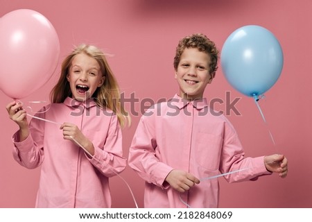 beautiful, happy children boy and girl stand on a pink background holding pink and blue balloons in their hands