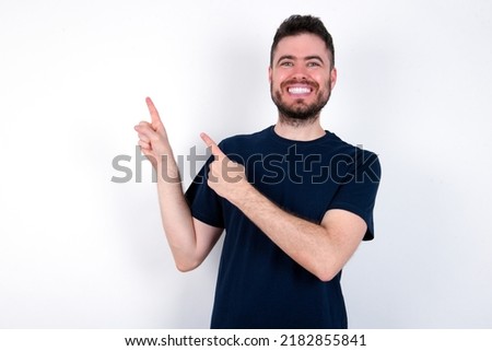 Young caucasian man wearing black T-shirt over white background indicating finger empty space showing best low prices, looking at the camera