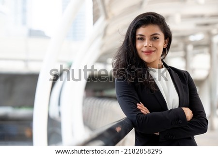 Powerful hispanic woman in business suit standing with arm crossed ourdoors in the city Royalty-Free Stock Photo #2182858295