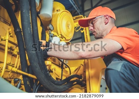 Closeup of Male Caucasian Worker Checking and Fixing an Engine in Construction Machine. Workshop in the Background. Heavy Duty Industrial Equipment Theme. Royalty-Free Stock Photo #2182879099