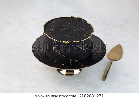 Chocolate cake with black icing, decorated with gold sequins on a white background. A picture for a menu or a catalog of confectionery products.