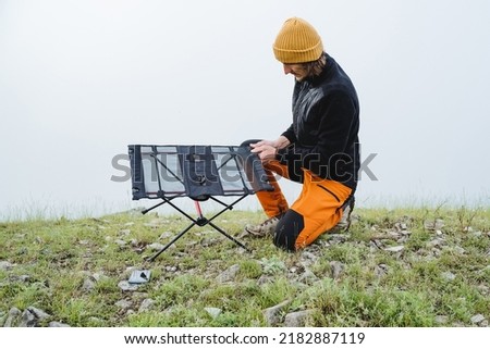 The guy collects a frame table for camping in nature, assembling camping equipment, picnic in the mountains, fog. High quality photo