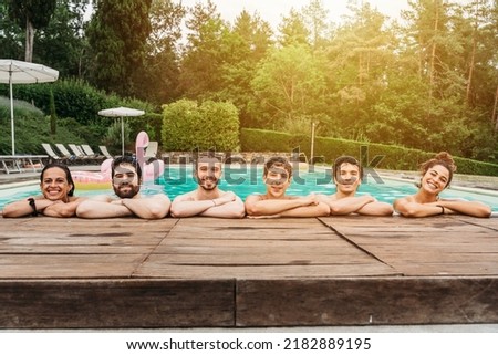 Portrait of a group of young friends at the hotel pool where spend their summer vacation at sunset - People in swimwear suits relax and have fun together outdoors near the hotel - Copy space