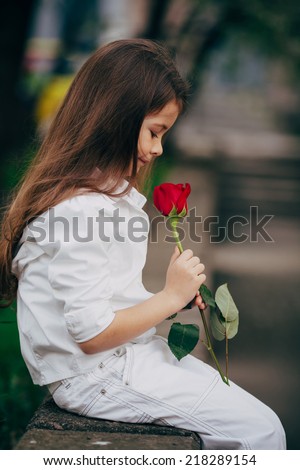 little and pretty girl smell rose outdoor in white suit