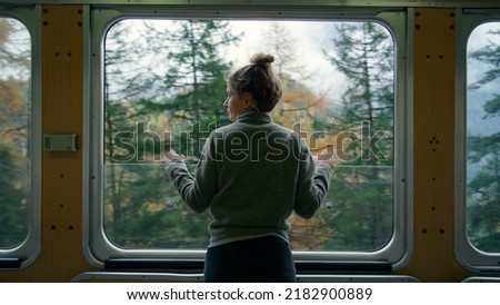 Cinematic and symmetrical beautiful shot of female traveler, travel blogger and inspired adventurer hang out of train window, look at amazing landscape of autumn mountains Royalty-Free Stock Photo #2182900889