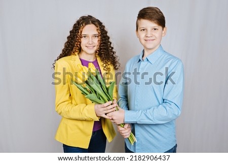 First love concept. Teen boy gives his girlfriend a bouquet of yellow tulips on white background.