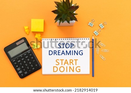 stop dreaming start doing. Text written on notepad page, calculator, pen, stationery on orange background. conceptual image