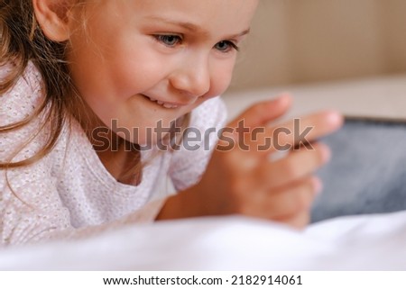 Close up happy little child playing online game on gadget, using mobile applications, having fun with cellphone alone at home