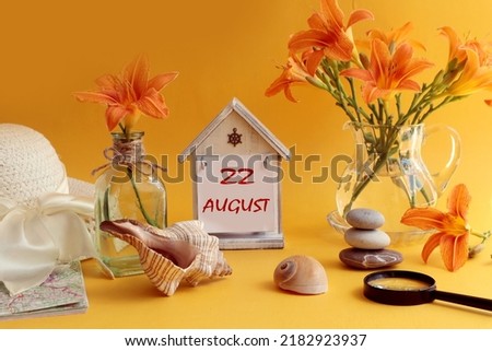 Calendar for August 22: decorative house with numbers 22, name of the month august in English, bouquets of daylilies, sea shells and stones, summer hat on an orange background, side view