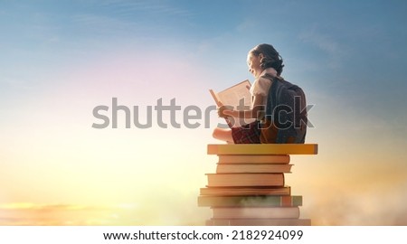 Back to school! Happy cute industrious child sitting on the tower of books on background of sunset sky. Concept of education and reading. The development of the imagination. Royalty-Free Stock Photo #2182924099