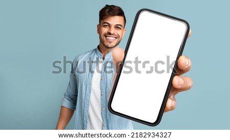Smiling Handsome Arab Guy In Casual Showing Mobile Phone With White Blank Screen For Advertisement, Recommending Mobile Dating Application, Panorama With Free Space, Mockup, Colllage Royalty-Free Stock Photo #2182934327