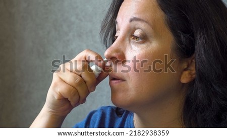 A woman treats a runny nose. Using a medicated spray Allergy. The cure for the disease. Cold symptoms. Infectious virus. Covid. Coronovirus. Indoors. Close-up. Royalty-Free Stock Photo #2182938359
