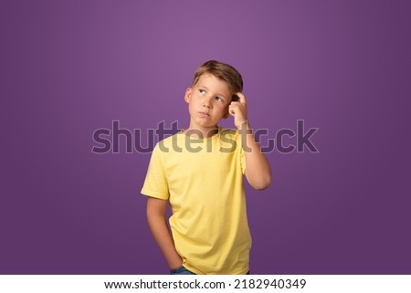 Thoughtful preteen kid boy standing with puzzled serious expression, making choise thinking against purple background. Studio shot Royalty-Free Stock Photo #2182940349
