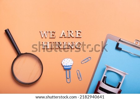 Wooden letters with phrase we are hiring on color background with magnifying glass, clip-board and stamp top view. Search worker concept.