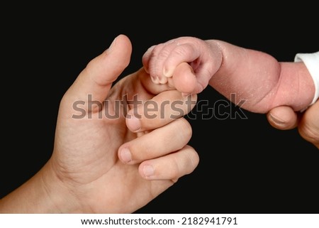 The small hand of a newborn caucasian baby grasps the hand of an adult person. Royalty-Free Stock Photo #2182941791