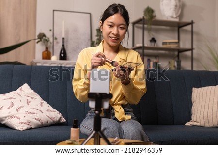Beauty Blog. Asian Female Blogger Making Makeup Filming On Cellphone Sitting On Sofa At Home. Woman Advertising Cosmetics Products. Professional Blogging Concept. Selective Focus
