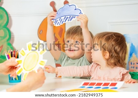 Little cute boy in kindergarten class hold the cart with weather rain card in hand showing to teacher who holds sun image