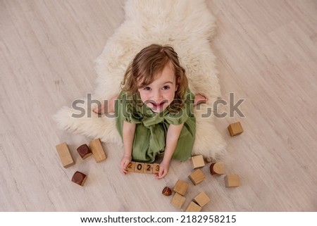 Top view of girl who holds wooden cubes with the numbers 2023 in her hands. The child plays in the construction of the tower. Active home games. Lifestyle kids education concept. Copy space, close up