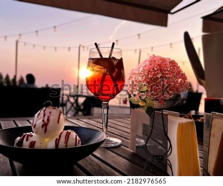 sunset at sea flowers in decorative  flowers cup ,ice cream and and glass of juice on wooden table top in beach cafe  view in pink sky and sea nature landscape 