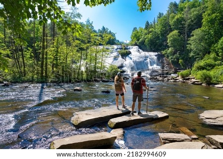 Couple standing on the rock enjoying beautiful waterfall view.Friends relaxing on hiking trip.High Falls  of Dupont State Forest in Brevard. Blue Ridge Mountains, near Asheville, North Carolina, USA. Royalty-Free Stock Photo #2182994609