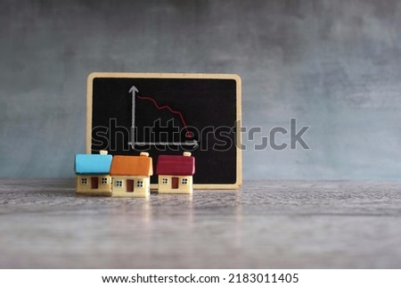 Toy house and chalkboard with downward arrow graph. Home sales market decrease loss concept.