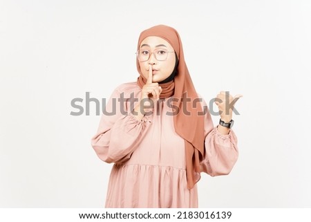 Shh gesture, Presenting and Pointing Side Product Using Thumb of Beautiful Asian Woman Wearing Hijab Isolated On White Background