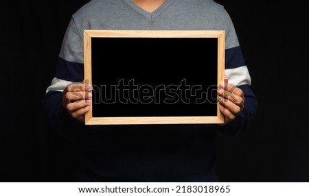 Close-up of hands holding a blank mini blackboard while standing on a black background. Space for text
