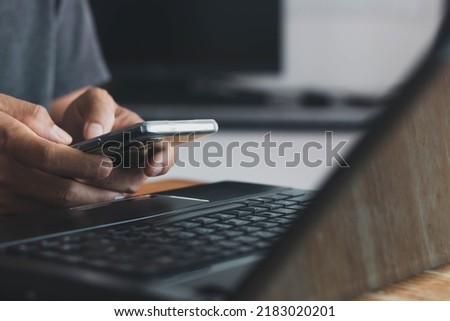 Man hand holding smart phone, and Businessman's hand using a smartphone for SMS messages with a laptop computer in an office. business, lifestyle, technology, and Social media network concept.