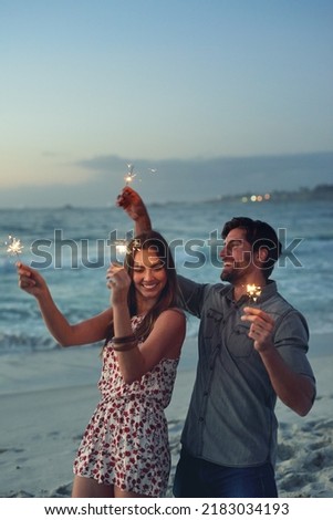 happy couple holding sparklers celebrating new years eve on beach at sunset with sparkle firework Royalty-Free Stock Photo #2183034193