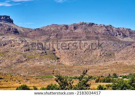 Natural landscape view of mountain in nature. Scenic look of rocky hills and grassy terrain on a sunny day in the outdoors. Big blue sky background with greenery and small separated clouds outside.