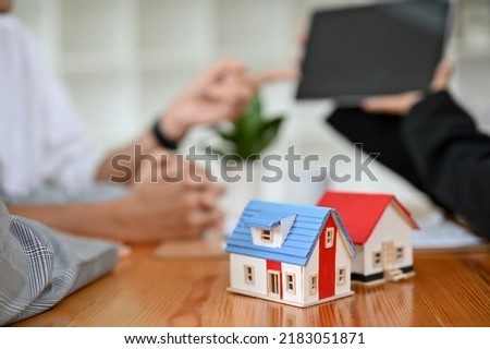 A house model is on the meeting table over a blurred background with a real estate agent and client having a meeting. cropped image
