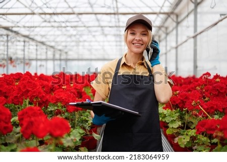 Mature female employed in greenhouse with flowers talking on mobile phone