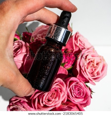 Rose essential oil. A bottle of rose oil with pink flowers. Organic natural bio-oil. oil in a glass bottle with a pipette and pink rose flowers in the girl's hand. Selective focus.
