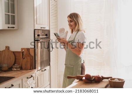 charming young woman in chef's apron puts apple pie in the oven and takes pictures on phone