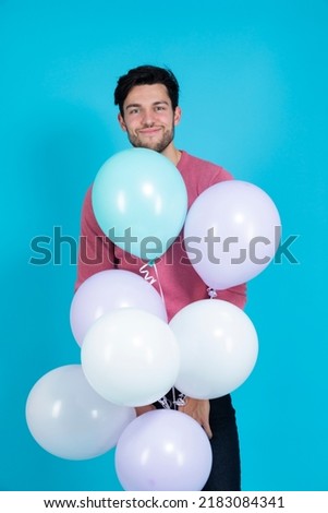 Positive Caucasian Guy Handsome Brunet Man With Bunch of Colorful Air Balloons in Pink Jumper Standing On Blue Background.Vertical Image
